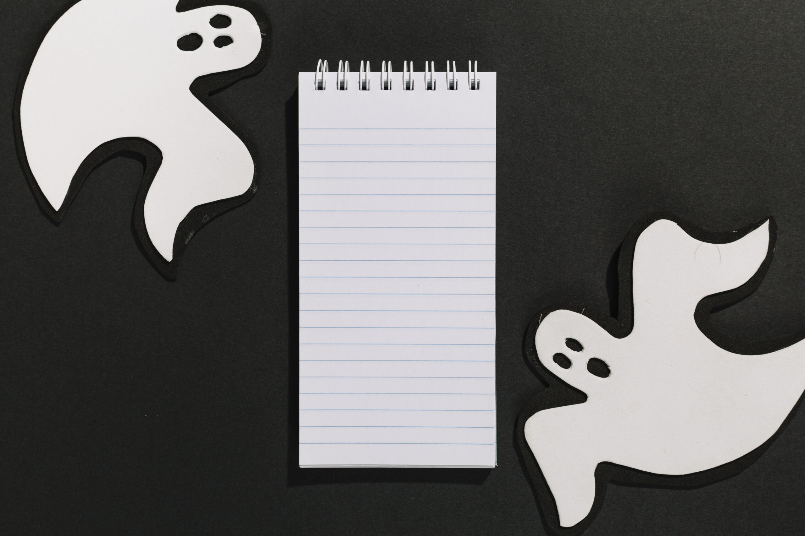 Fantasmas decorativos de papel junto a un cuaderno, representando el concepto de ghostwriting y la creación anónima de contenidos.