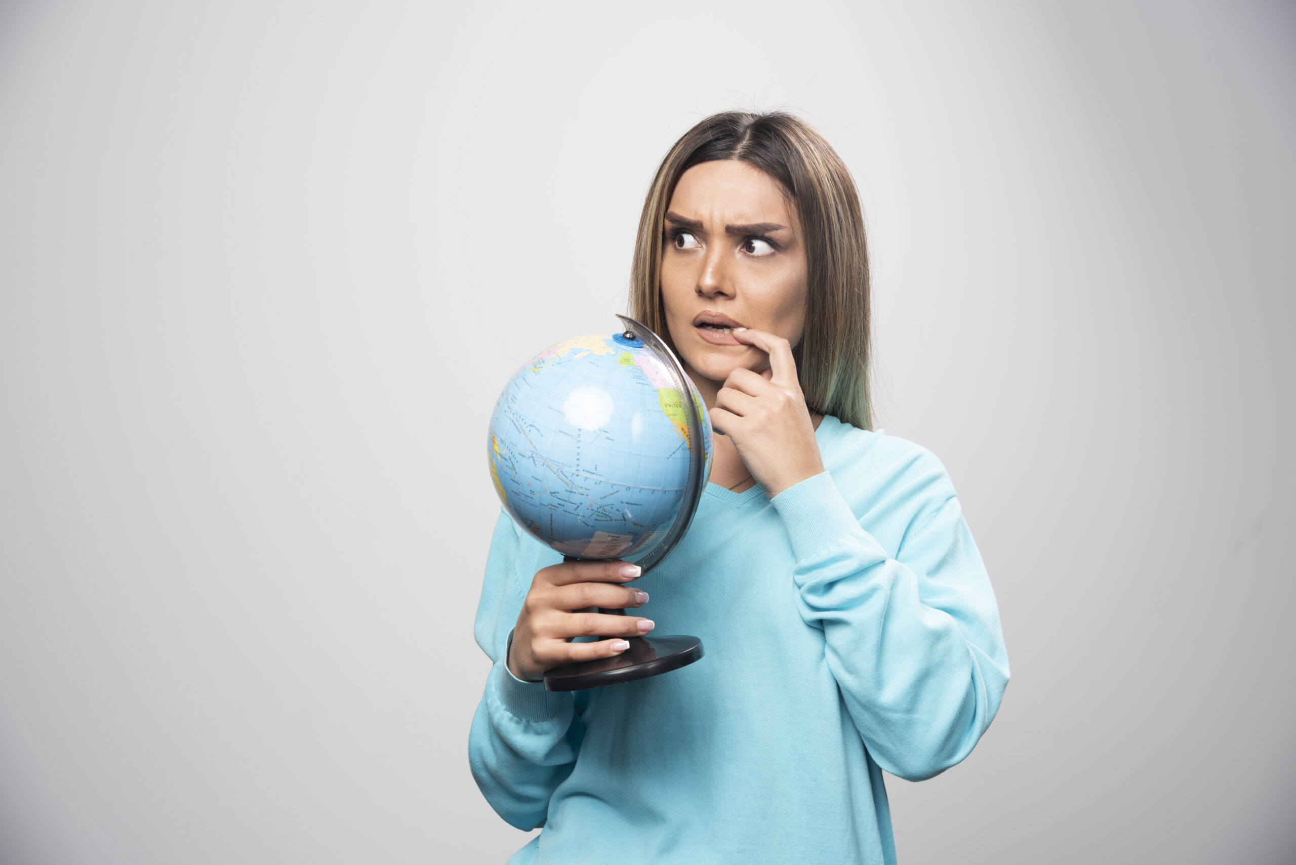 Chica rubia sosteniendo un globo terráqueo mientras piensa, relacionada con estrategia global y marketing digital.
