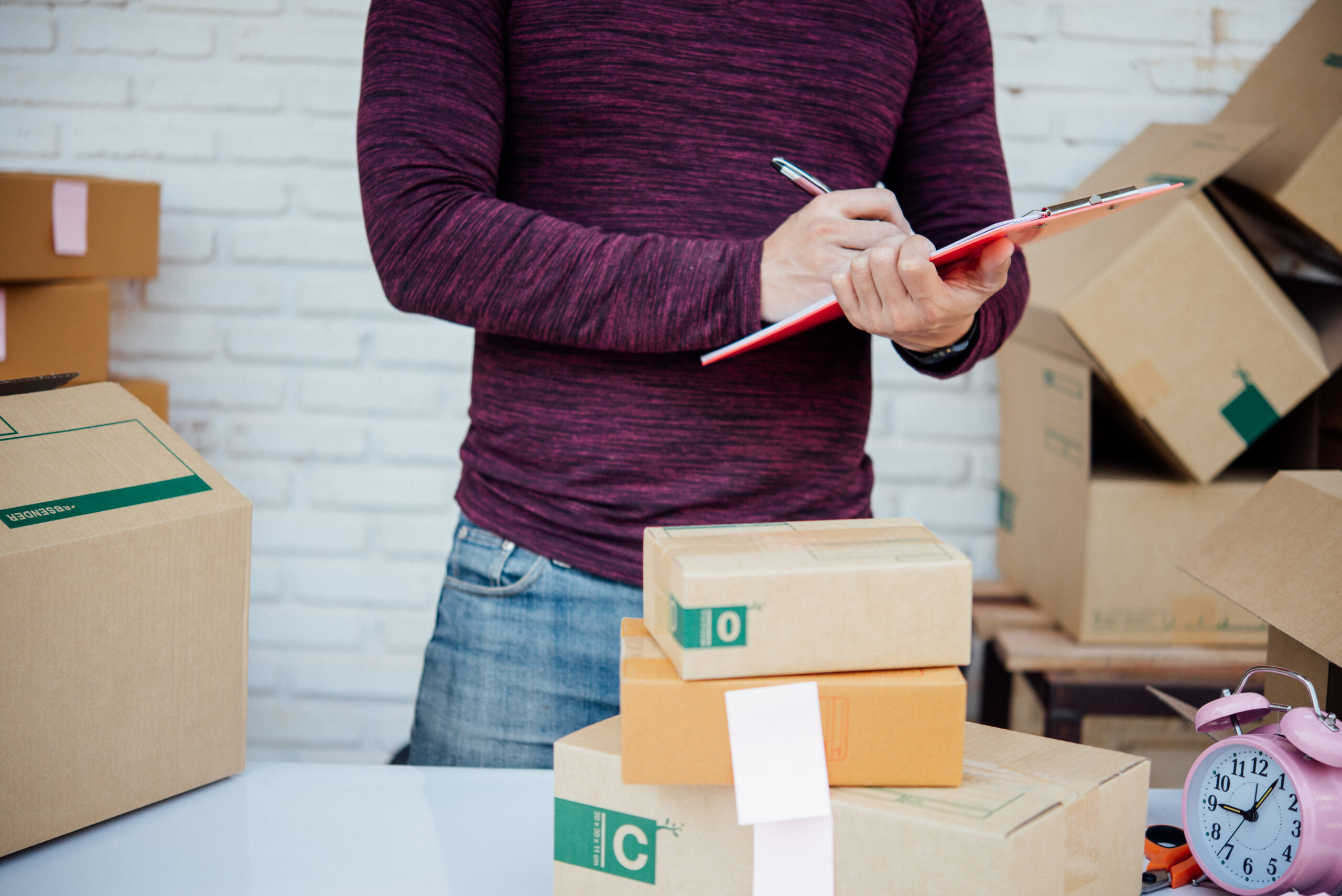 Hombre trabajando con documentos y paquetes en un entorno de logística y gestión de envíos.