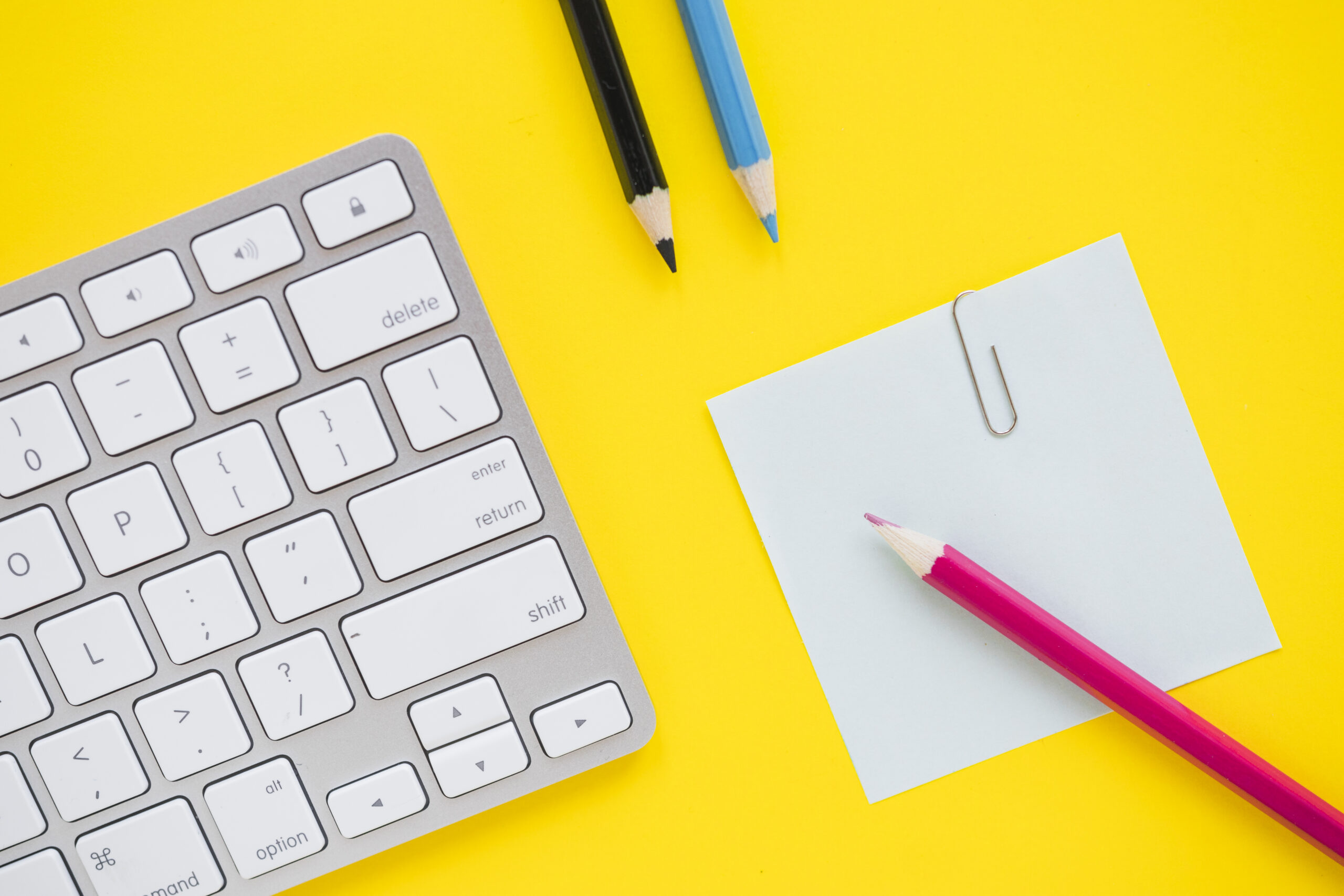 Teclado de ordenador con notas adhesivas y bolígrafos, representando la planificación de copywriting y contenido digital.