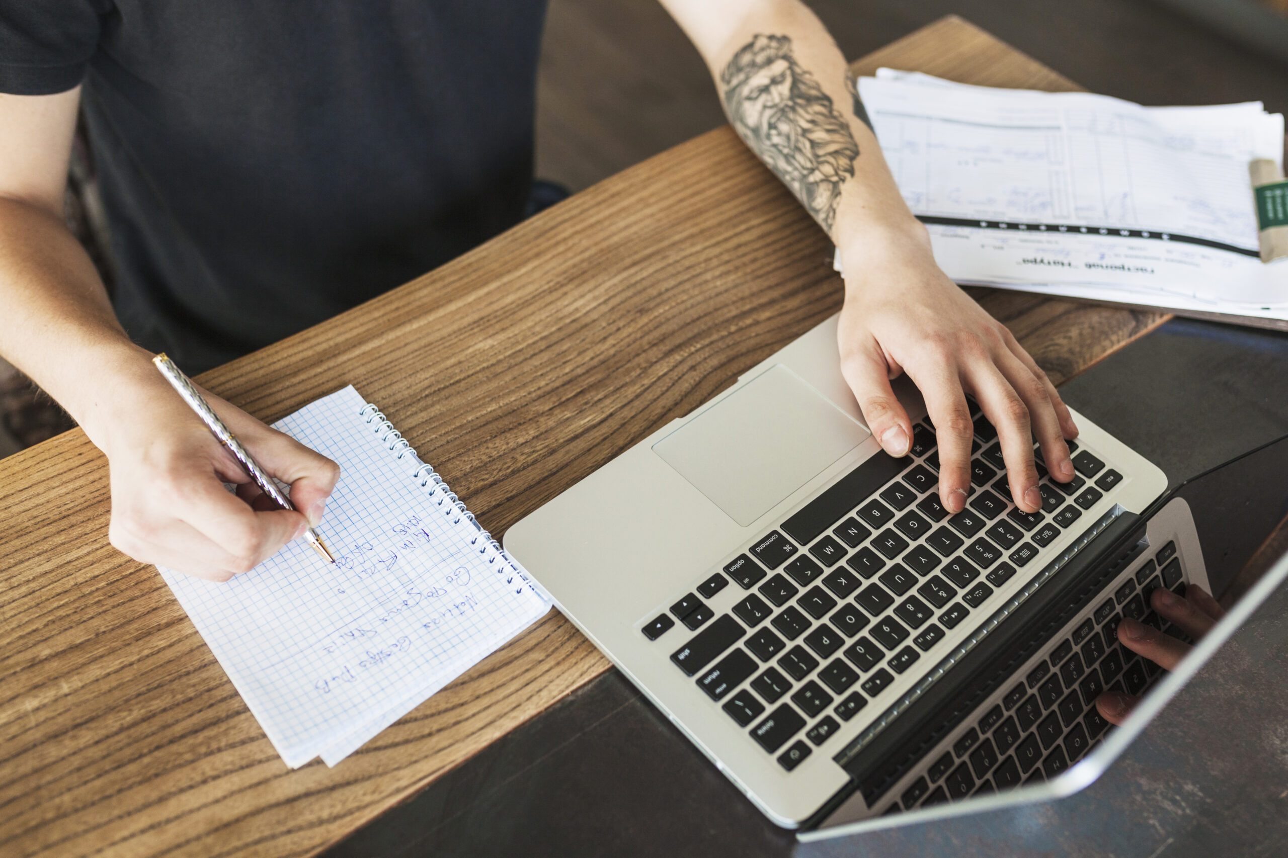 Persona escribiendo ideas de copywriting en un cuaderno mientras trabaja con un portátil.