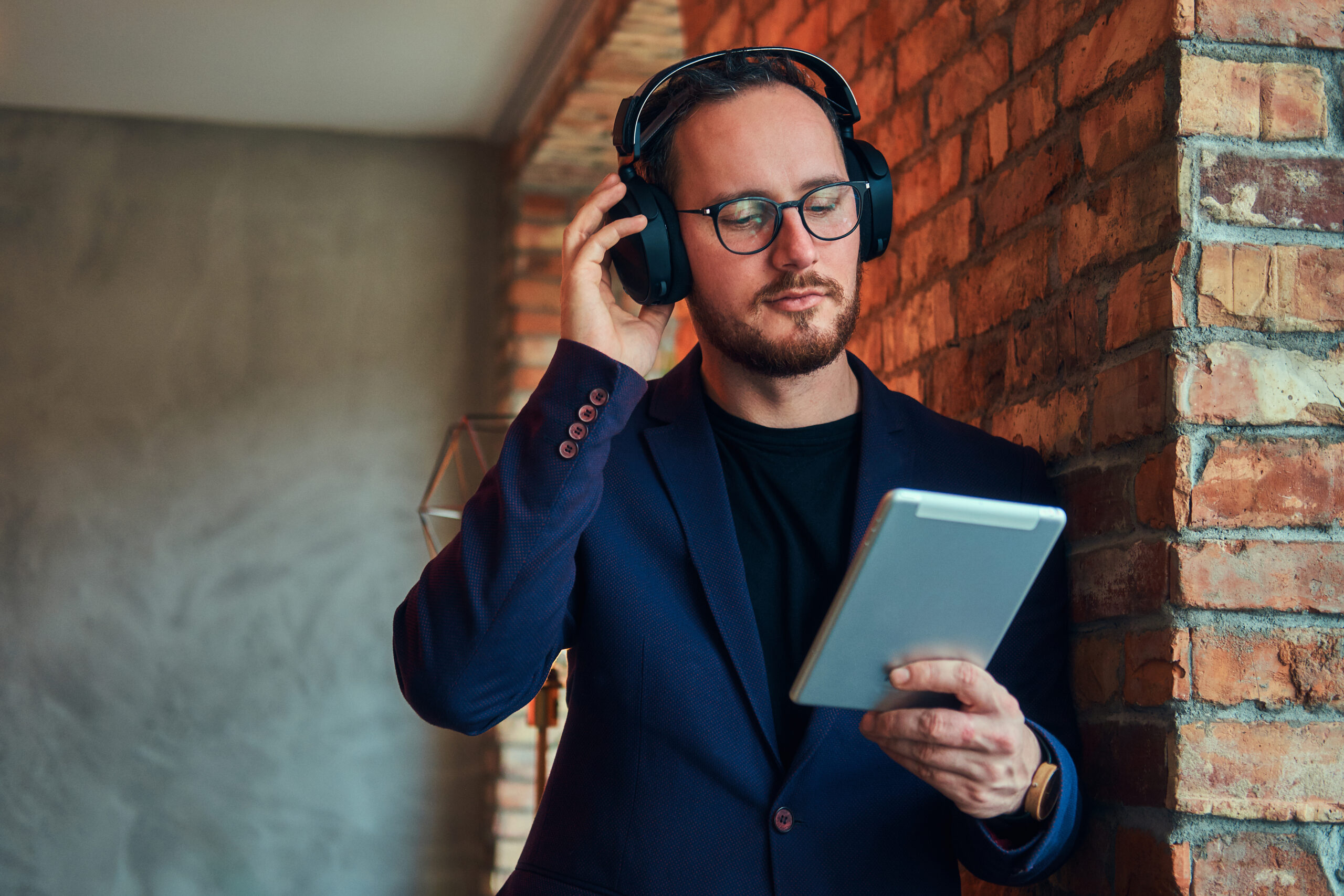 Hombre escuchando música con auriculares mientras usa una tablet, representando el branding sonoro en entornos digitales.