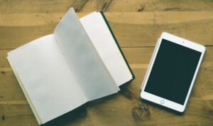 Tableta y cuaderno sobre una mesa de madera para planificar el diseño y la creación de la portada de un libro o eBook.