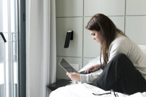 Mujer utilizando un ordenador portátil en una habitación de hotel para consultar información y realizar una reserva.