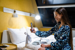 Mujer en una habitación de hotel elegante utilizando un teléfono móvil sobre la cama.